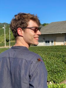 Alex has a dragonfly on his shoulder and is next to a tea field