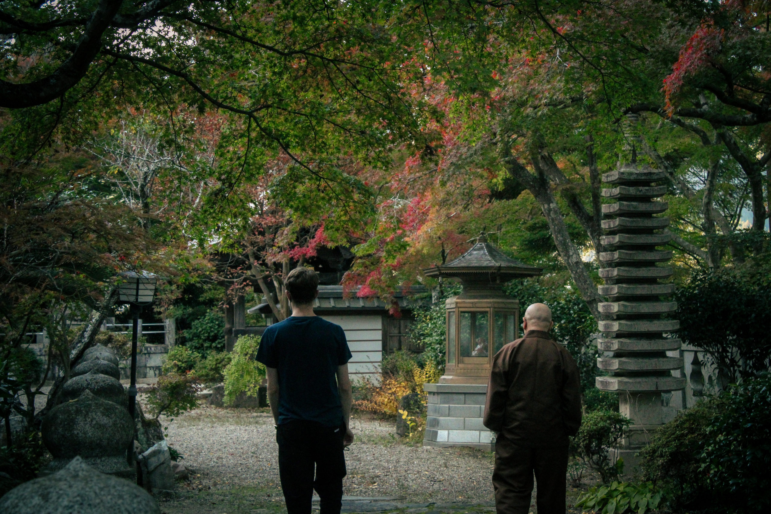 Alex and Ozeki-san face away from the camera. They look off into the distance at the scenery of Shouohouji. The trees are ripe with fall colors.