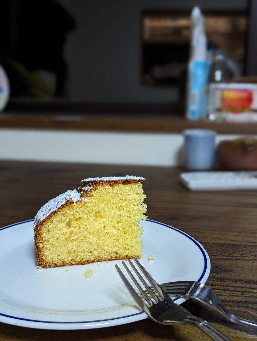 A slice of yuzu olive oil cake on a white plate with 2 forks
